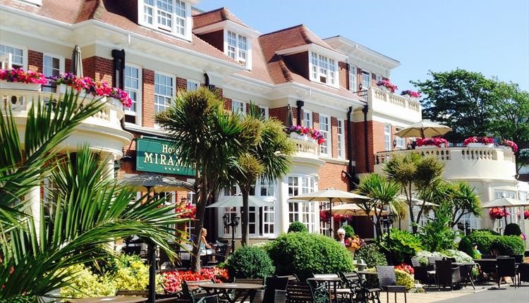 Front of the Miramar Hotel and gardens with table and chairs basking in the sun 